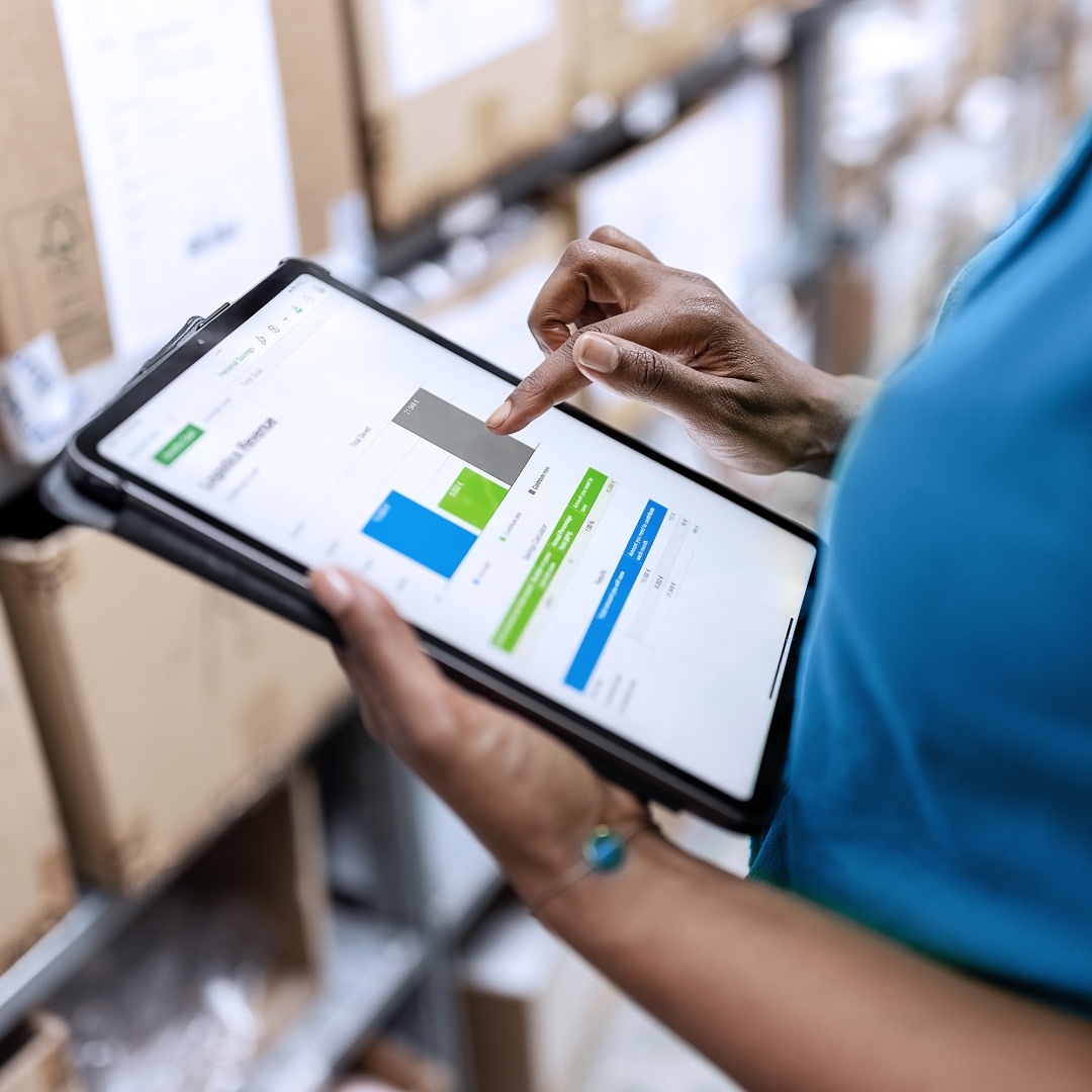 Am Tablet tippende Hände, Lagerraum im Hintergrund steht für digitalen Produktpass