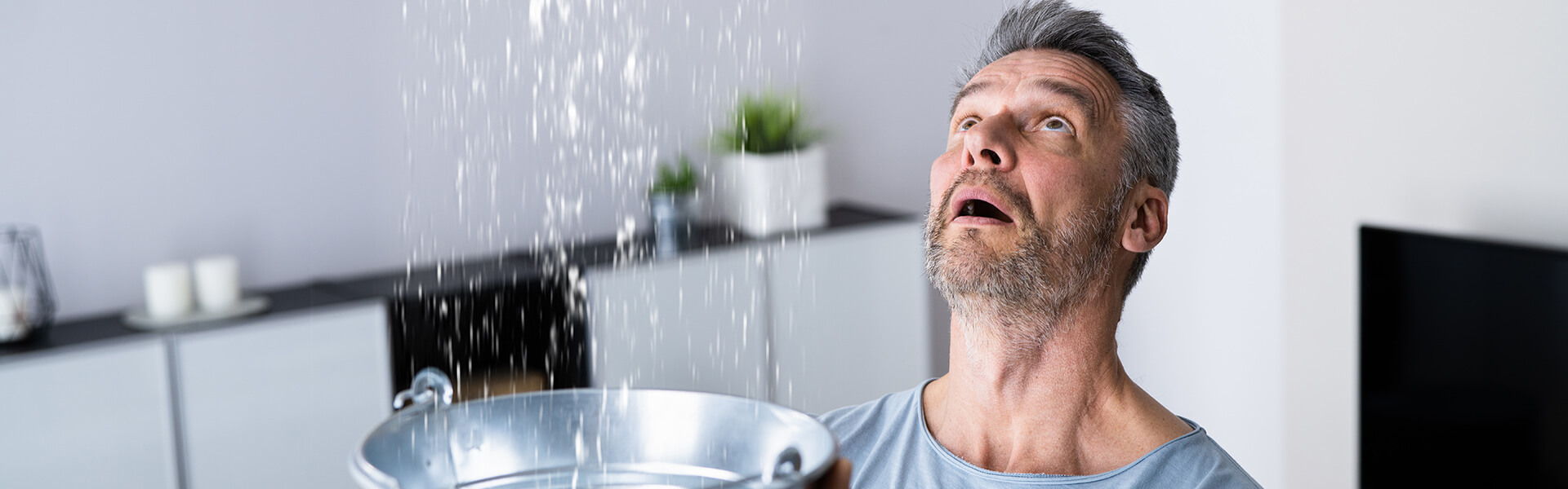 Un homme place un sceau sous une infiltration d'eau au plafond